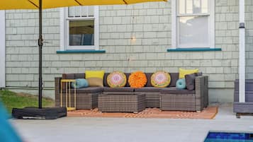A patio area with a wicker sofa, colorful cushions, a yellow umbrella, and a pool.
