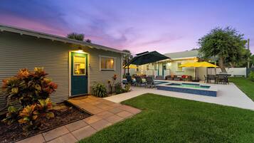 A residential property with a swimming pool, outdoor seating, and a well-maintained lawn.