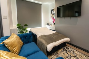 Ein modernes Schlafzimmer mit einem Bett, einem blauen Sofa, einem Fernseher und einer Pflanze.