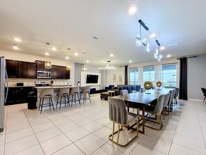 A modern kitchen with a dining area, a flat-screen TV, and a large window. - Windsor Island | 10BR Luxury Haven + Game Room (Davenport)