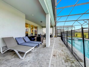 A covered outdoor area with lounge chairs, a pool, and a view of the landscape. - Windsor Island | 10BR Luxury Haven + Game Room (Davenport)
