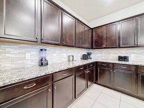 A kitchen with dark wooden cabinets, a granite countertop, and a tiled backsplash. - Windsor Island | 10BR Luxury Haven + Game Room (Davenport)
