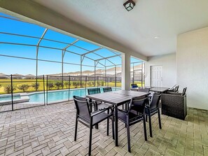 A covered patio with a pool view, outdoor table and chairs, and a door leading to the interior. - Windsor Island | 10BR Luxury Haven + Game Room (Davenport)
