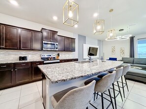 A modern kitchen with dark wood cabinets, a granite island, and bar stools. - Windsor Island | 10BR Luxury Haven + Game Room (Davenport)