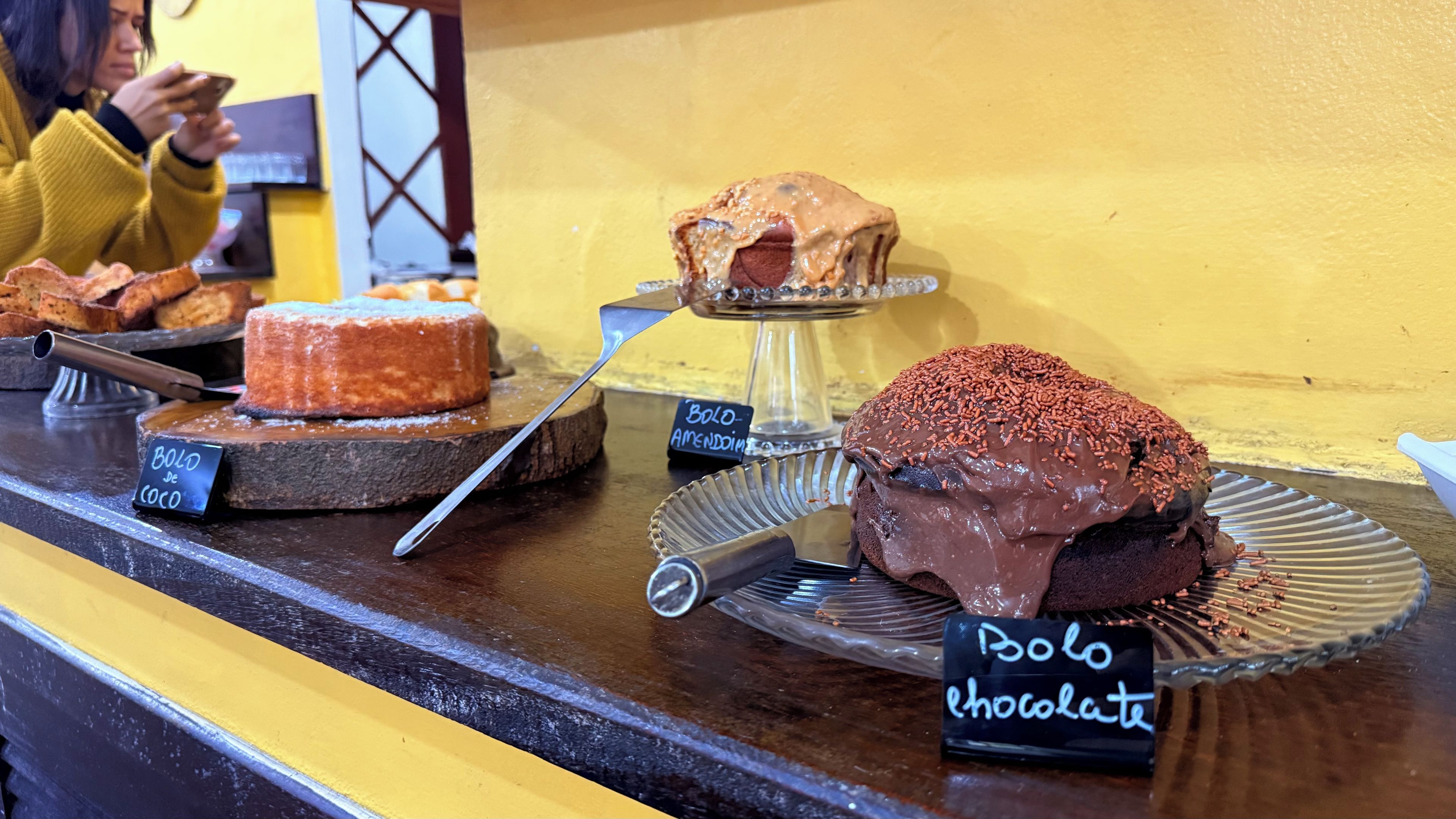 A dessert display with various cakes and a sign indicating 'Bolo de coco' and 'Bolo chocolate'.