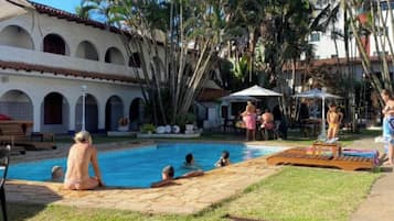 A pool area with people relaxing, surrounded by palm trees and a building with arches.