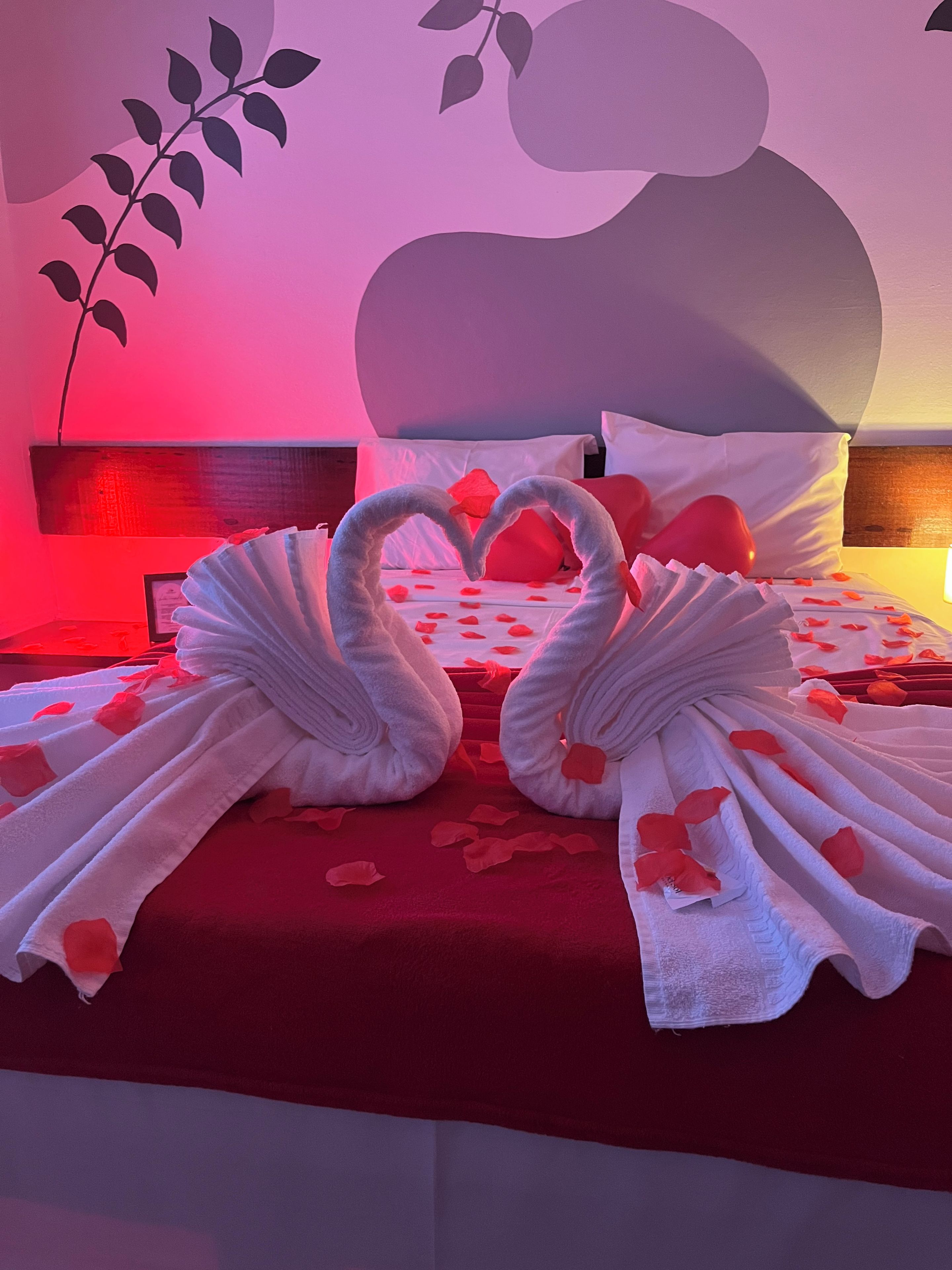 Una cama con colcha roja, almohadas blancas y una disposición de toallas con forma de corazón.