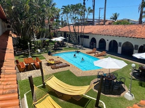 A swimming pool area with lounge chairs, a hammock, and a patio with tables and umbrellas. - Pousada Puerta del Sol (Rio das Ostras)
