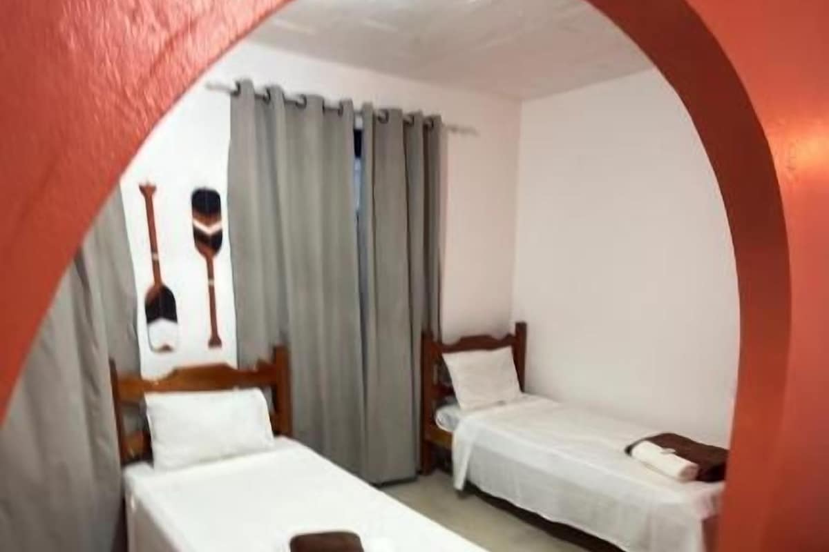 A room with two beds, a wooden headboard, a white curtain, and a red archway.