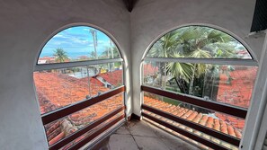 A room with two large arched windows offering views of red-tiled roofs and palm trees.