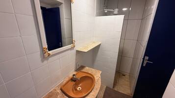 Une salle de bain avec des murs recouverts de carreaux blancs, un lavabo marron, un miroir avec un cadre en bois et une porte bleue.