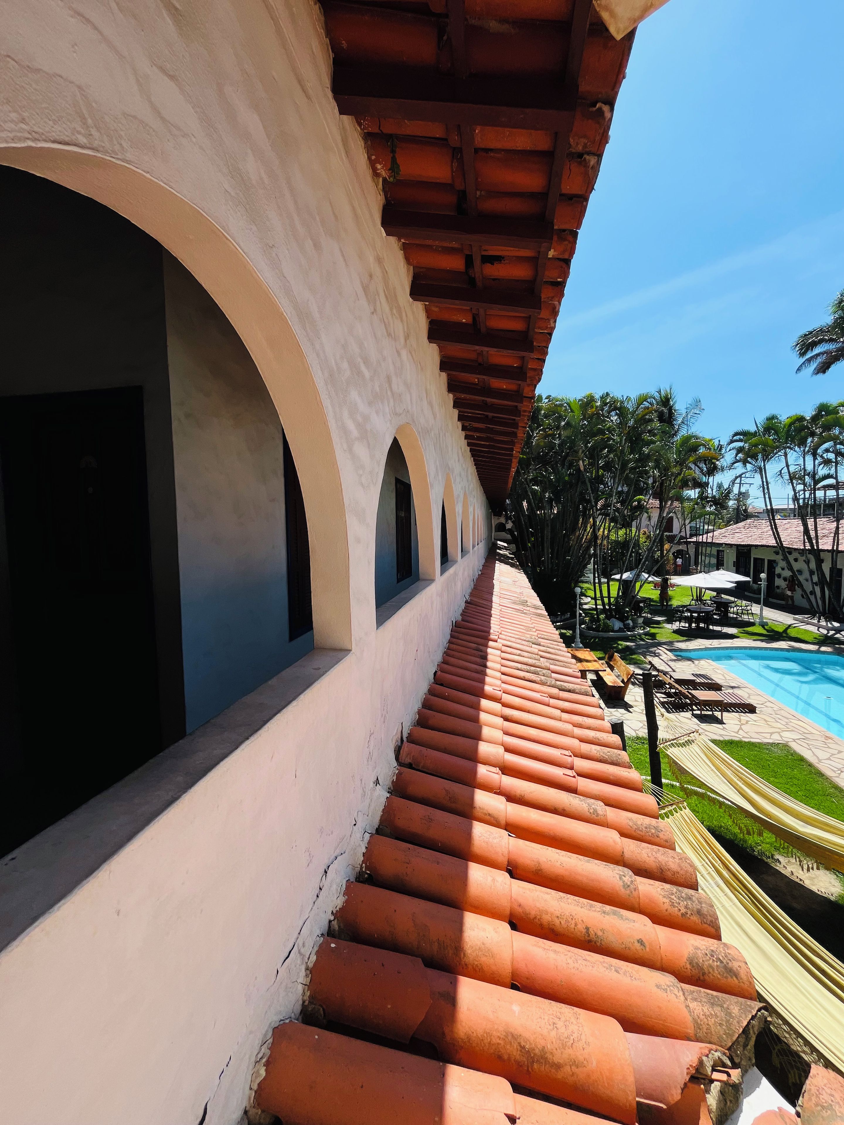 A hotel corridor with a pool area, outdoor seating, and palm trees.
