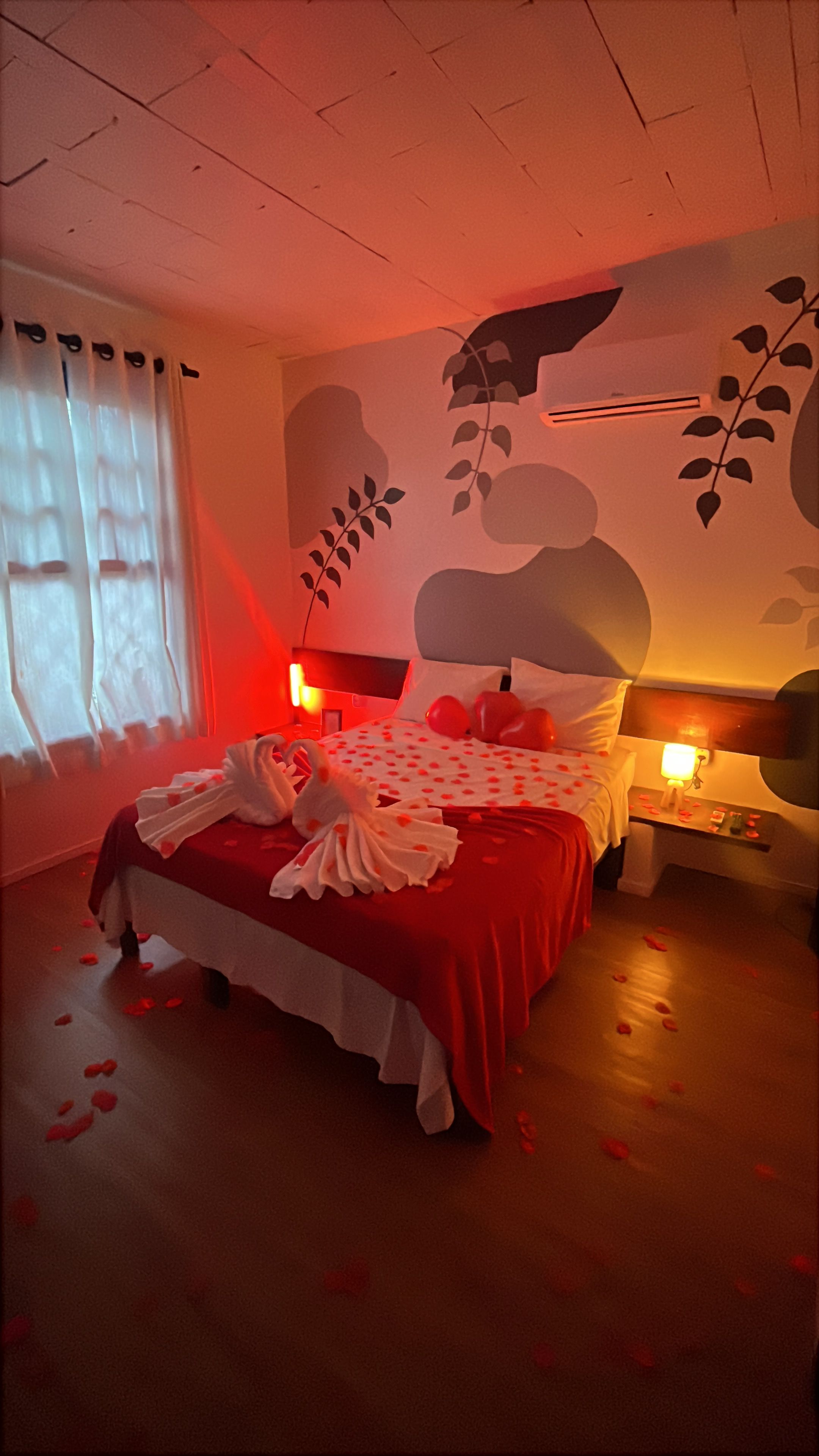 A hotel room with a bed, a nightstand, a wall-mounted air conditioner, and a window with curtains.
