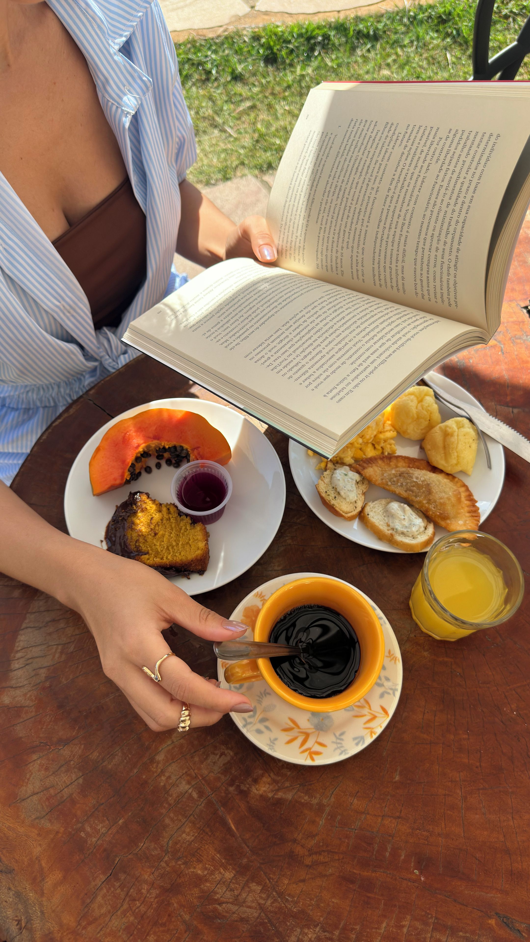 A person reading a book at a table with a plate of food, a cup of coffee, and a glass of juice.