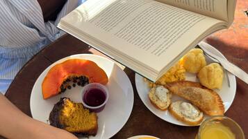 A person reading a book at a table with a plate of food, a cup of coffee, and a glass of juice.