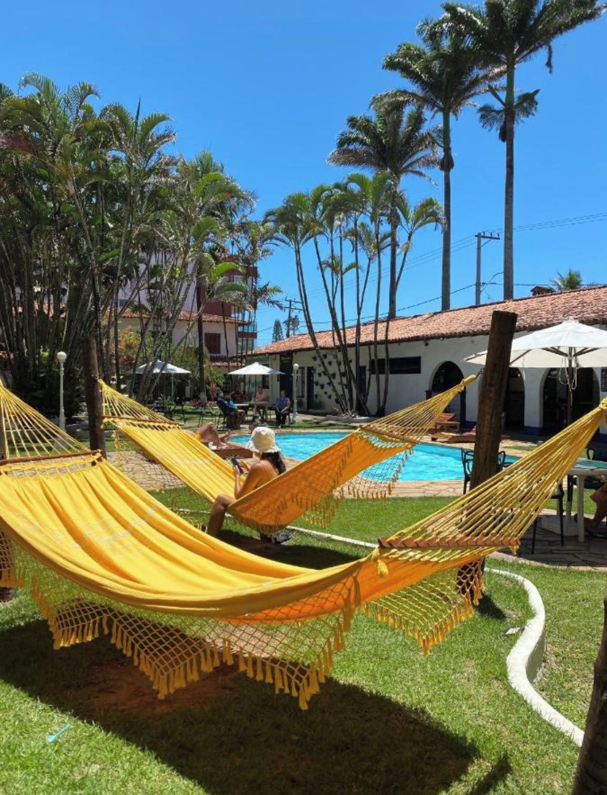 A pool area with yellow hammocks, palm trees, and a building with a tiled roof.