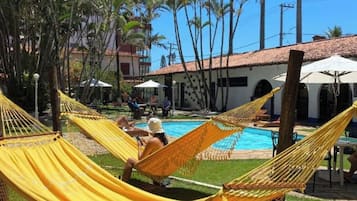 A pool area with yellow hammocks, palm trees, and a building with a tiled roof.