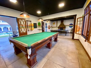 A pool table in a room with a tiled floor, pendant lighting, and a view of a courtyard.