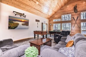A cozy living room with a wooden ceiling, a large fish mounted on the wall, a foosball table, a pool table, and a sofa with cushions. - Chain Of Lakes direct trail access / Free Firewood (Eagle River)