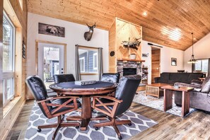 A cozy cabin interior with a round wooden table, leather chairs, a fireplace, and a large window. - Chain Of Lakes direct trail access / Free Firewood (Eagle River)