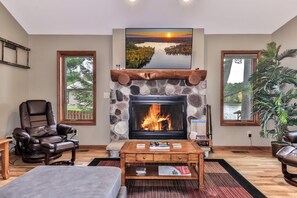 A living room with a stone fireplace, leather recliner, and a coffee table with books. - Eagle River Chain – Steps to Golf & Lake Life! (Eagle River)