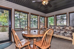 A dining area with a round wooden table and chairs, large windows, and a ceiling fan. - Eagle River Chain – Steps to Golf & Lake Life! (Eagle River)