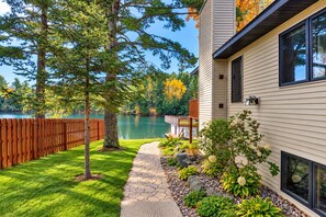 A house with a view of a lake, a wooden deck, and a stone pathway leading to the house. - Eagle River Chain – Steps to Golf & Lake Life! (Eagle River)
