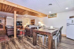 A cozy living room with a wooden ceiling, a dining area with a wooden table and metal chairs, and a kitchen with a refrigerator. - Secluded 3 Story Lake Front Home with large deck, private pier, C/A & More! (Eagle River)