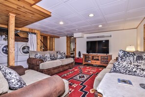 Ein Wohnzimmer mit einer Sofagarnitur, einem roten Teppich mit Muster, einem Fernseher und einer Holzbalkendecke.