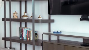 A modern living room with a TV mounted on the wall, a wooden cabinet, and a bookshelf with various items. - Península Sky Residence | Ixtapa Beachfront (Ixtapa Zihuatanejo)