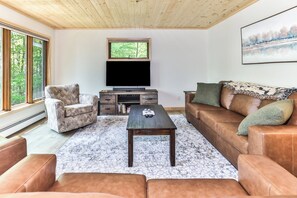Een woonkamer met een flatscreen televisie, een bruine leren bank, een gestreept fauteuil en een salontafel.