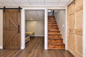 A hallway with a wooden staircase leading to a bedroom with a bed and a bench. - Lakefront | Newly Remodeled | Firewood | WIFI (Eagle River)