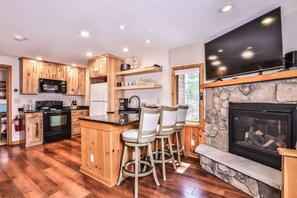 A kitchen with wooden cabinets, a stone fireplace, a flat-screen TV, and a bar area with stools. - Private Full Rec Lake Launch & Dock! Free Firewood (Eagle River)