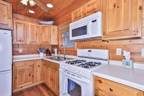 A kitchen with wooden cabinets, a microwave, a stove, and a refrigerator. - Sandy Bottom | Secluded | UTV/Snowmobile Access (conover)