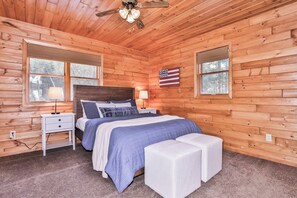 A wooden cabin bedroom with a bed, nightstands, a ceiling fan, and an American flag. - Sandy Bottom | Secluded | UTV/Snowmobile Access (conover)