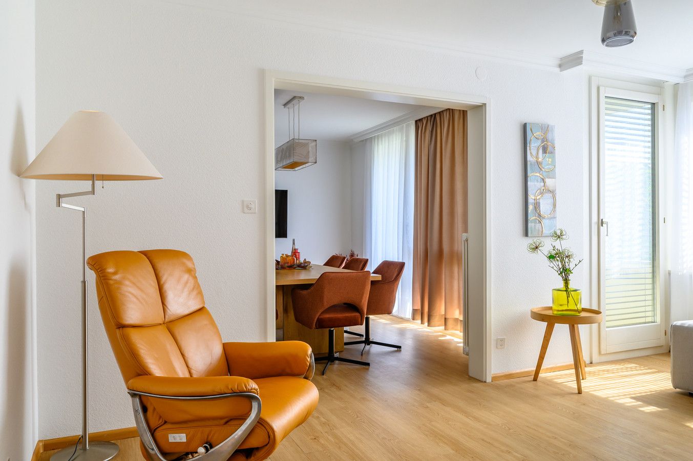 Ein modernes Wohnzimmer mit einem Ledersessel, einem Essbereich mit Tisch und Stühlen sowie einem kleinen Beistelltisch mit einer Vase.