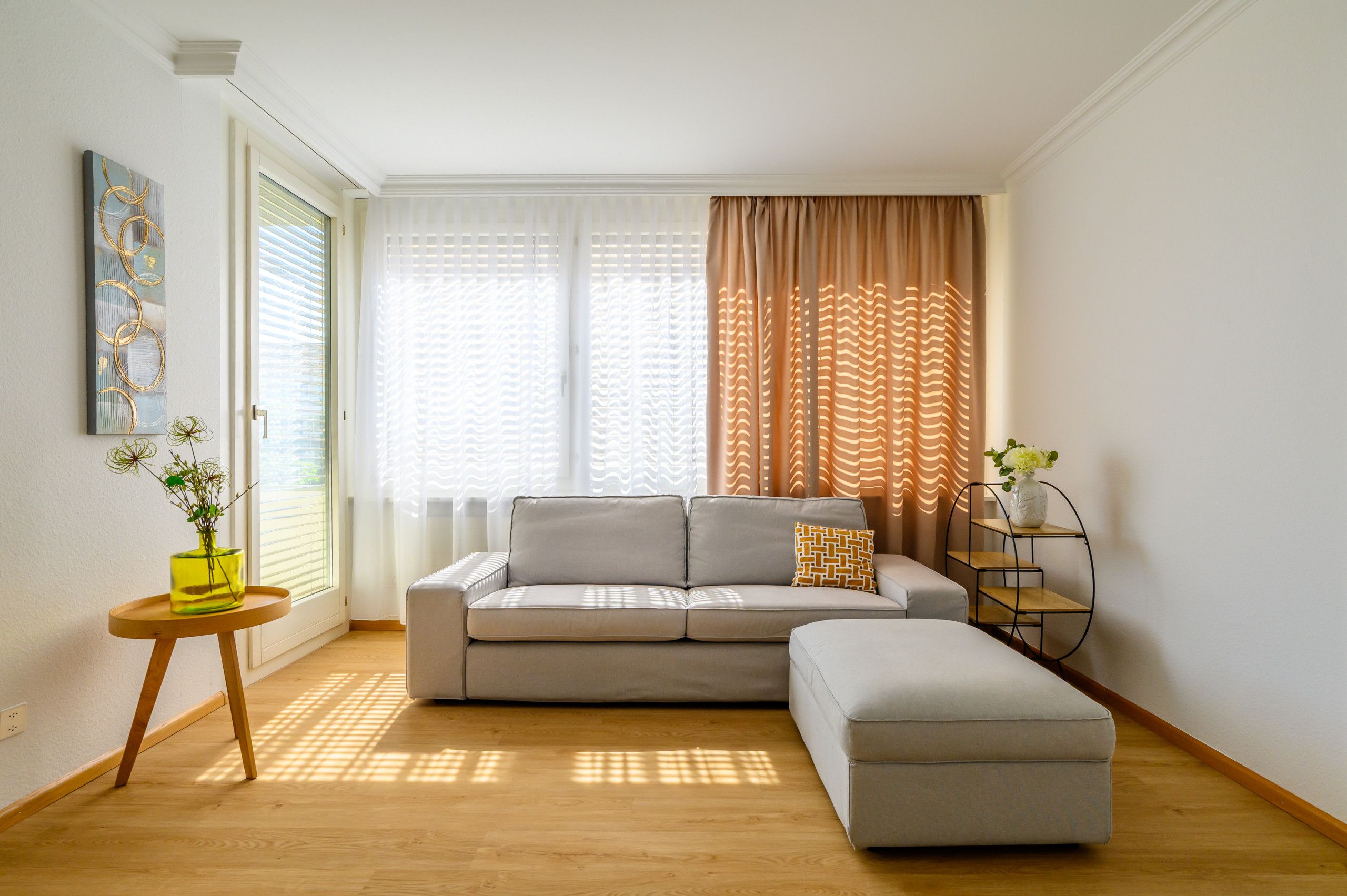 Un salon moderne avec un canapé, un pouf et une table d’appoint sur laquelle est posé un vase.