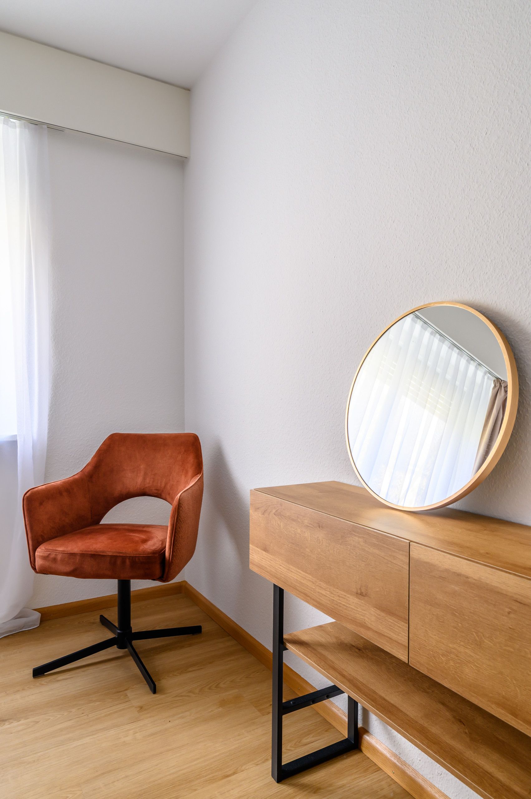 Ein Eckzimmer mit einem Holzstuhl, einem Holztisch und einem runden Spiegel an der Wand.
