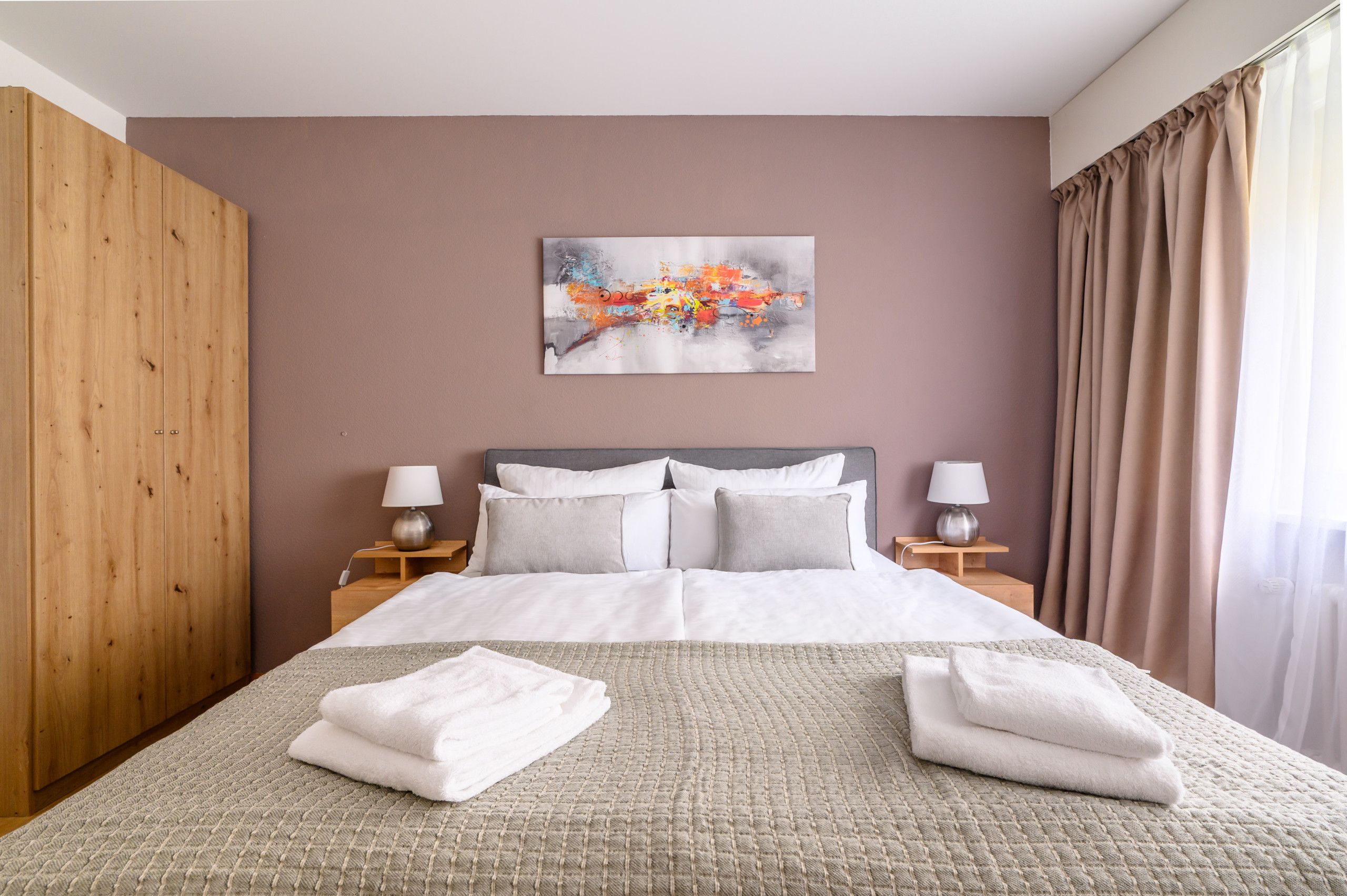 Une chambre d’hôtel avec un grand lit, deux tables de chevet avec des lampes, une armoire en bois et un tableau au mur.