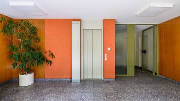 Un couloir avec un pot de plante, une porte avec une pancarte et un mur orné d’un motif texturé.