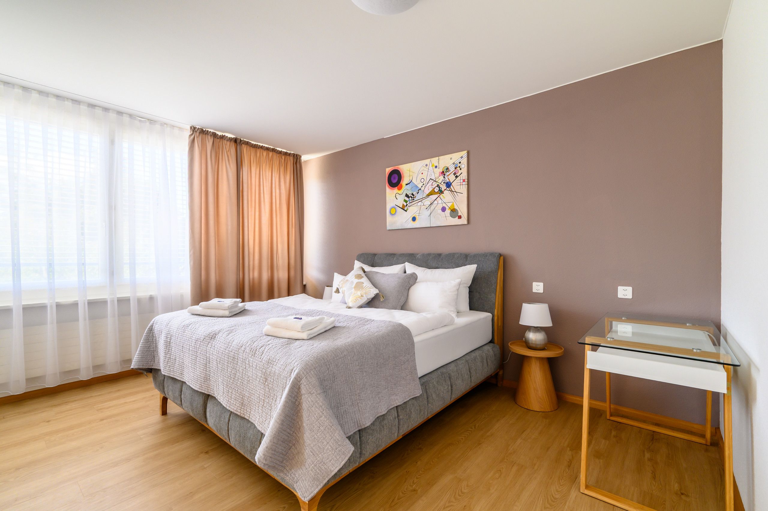 A modern bedroom with a bed, a bedside table, a lamp, and a painting on the wall.