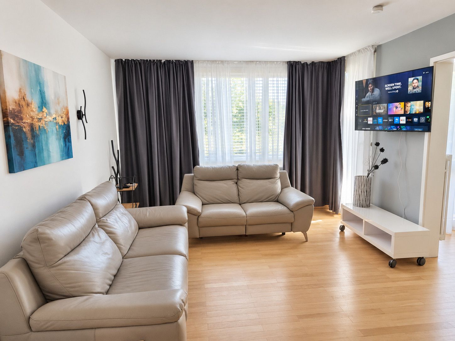 Un soggiorno moderno con due divani in pelle, una TV a schermo piatto e un'ampia finestra con tende.