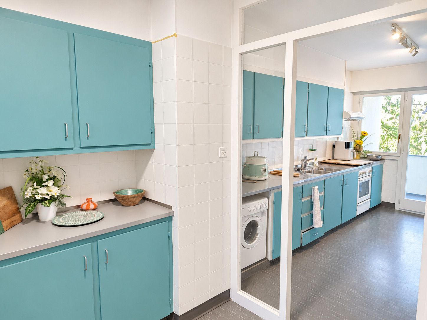 Une cuisine moderne avec des meubles de couleur turquoise, un lave-linge et une grande fenêtre.