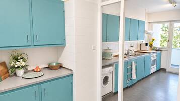 Une cuisine moderne avec des meubles de couleur turquoise, un lave-linge et une grande fenêtre.