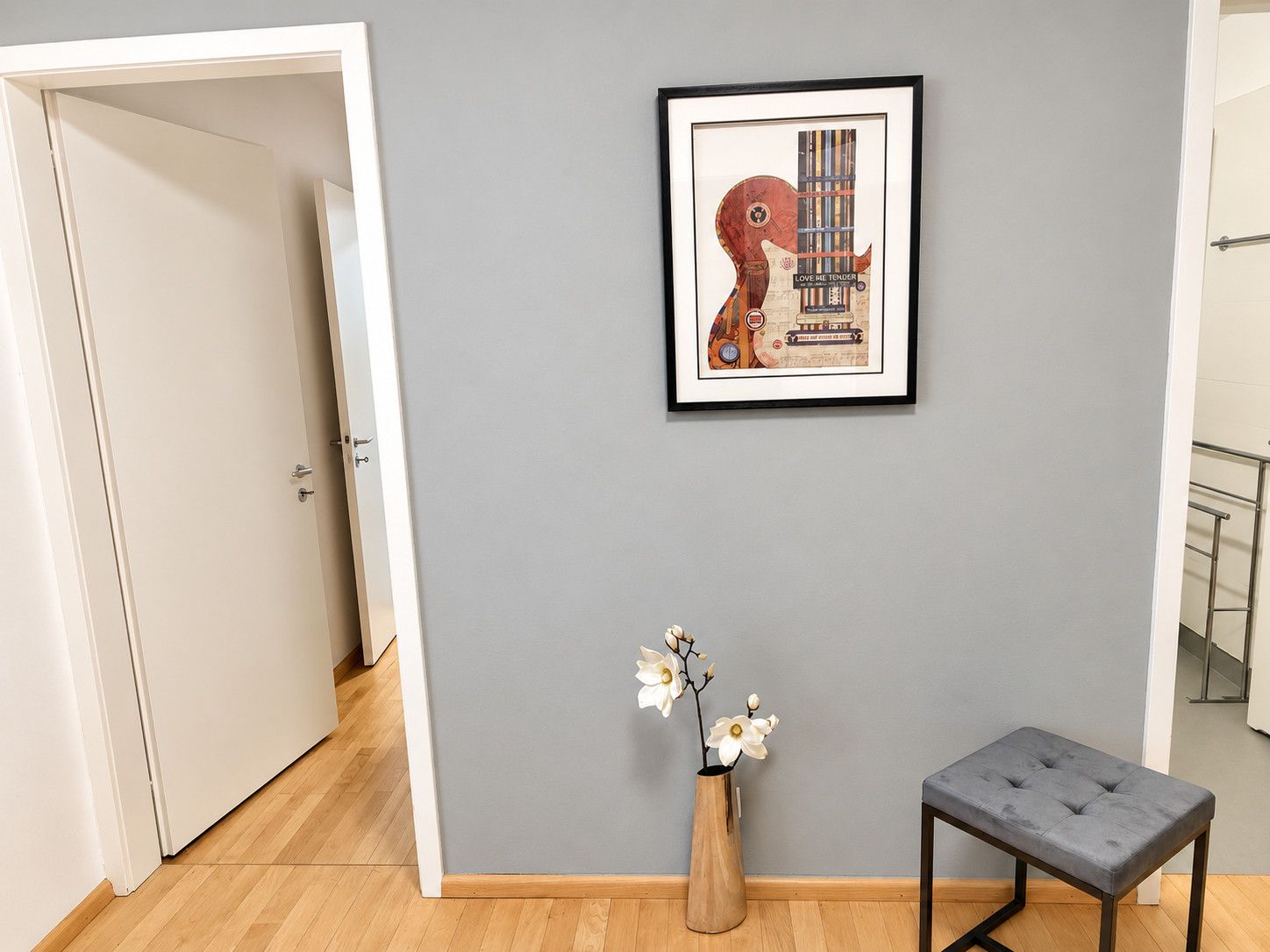 Une pièce avec un mur gris, une œuvre d’art encadrée, un vase en bois contenant des fleurs et un banc rembourré de couleur grise.
