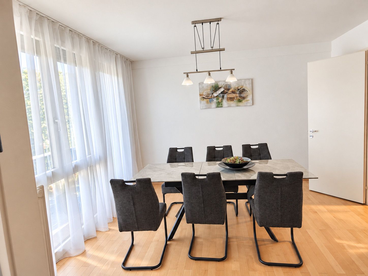 Un coin repas avec une table et des chaises, un tableau accroché au mur et une fenêtre avec des rideaux.