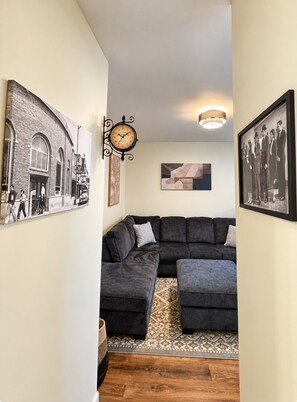 A living room with a sectional sofa, a wall clock, and framed pictures. - Sip, Stroll & Stay | Downtown Eagle River Apt (Eagle River)