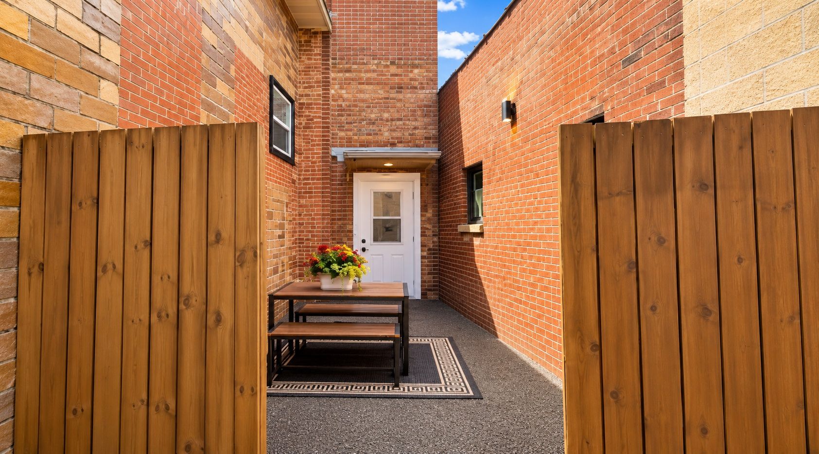 A narrow alleyway with a wooden gate, a brick wall, and a white door.