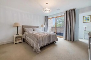 Ein Schlafzimmer mit Bett, Nachttischlampen, einem Schreibtisch und einem großen Fenster mit Vorhängen.