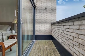 Ein Balkon mit einer Glastür, die zu einem Zimmer führt, Holzboden und Backsteinwand.